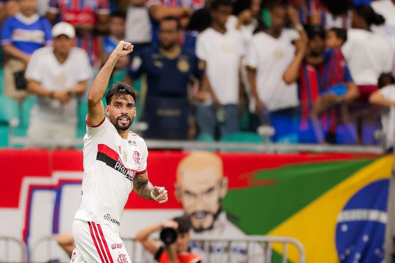Lucas Paquetá, com a camisa branca do Flamengo, ergue o punho fechado para comemorar, com a torcida ao fundo