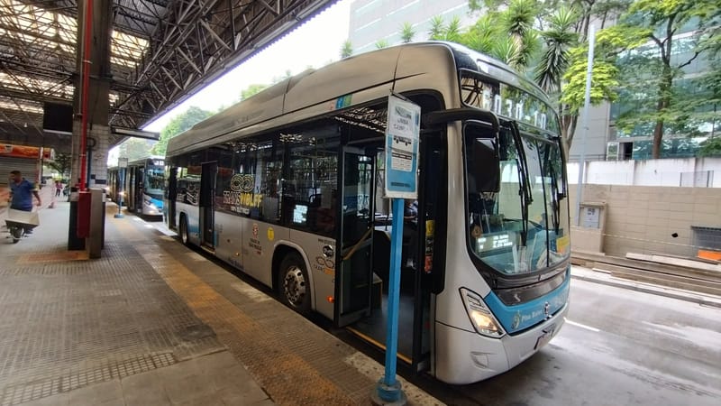 Ônibus elétrico da SPTrans, de lateral prateada e frente azul, com as portas abertas em plataforma coberta de terminal