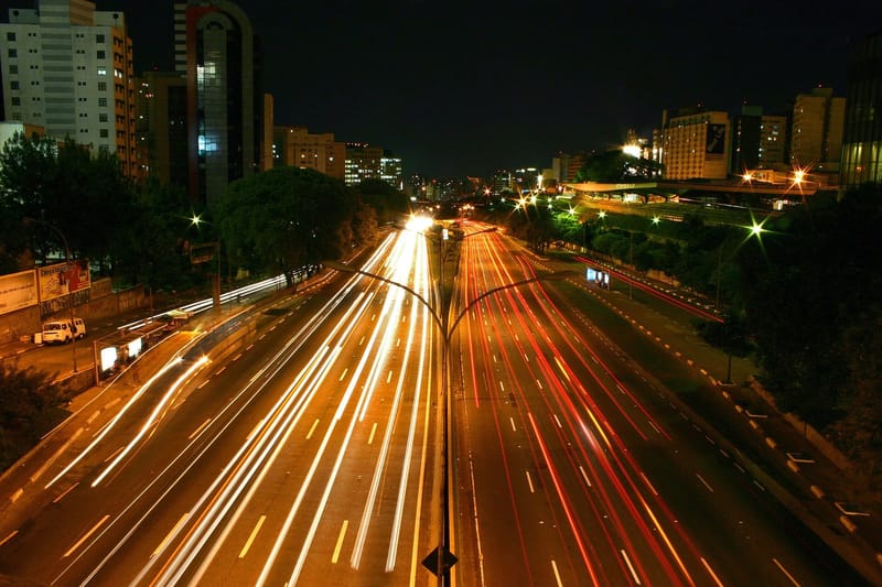 Avenida 23 de Maio, em São Paulo, à noite, com rastros de luz dos faróis dos carros nas pistas e prédios iluminados ao fundo