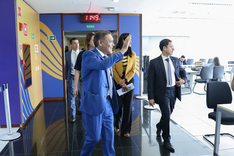 Kassio Nunes Marques, de terno azul e gravata listrada, acena sorrindo em um corredor do TSE