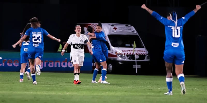 Jogadoras do Cruzeiro, de azul, comemoram em campo ao lado de uma adversária de branco, na Libertadores Feminina