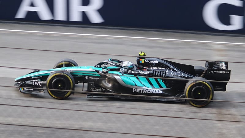 Carro verde-água da Mercedes de Fórmula 1 em alta velocidade na pista, visto de lado
