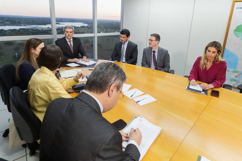 O ministro Bellizze e outros participantes sentados à mesa de reunião, numa sala do TSE com vista para Brasília