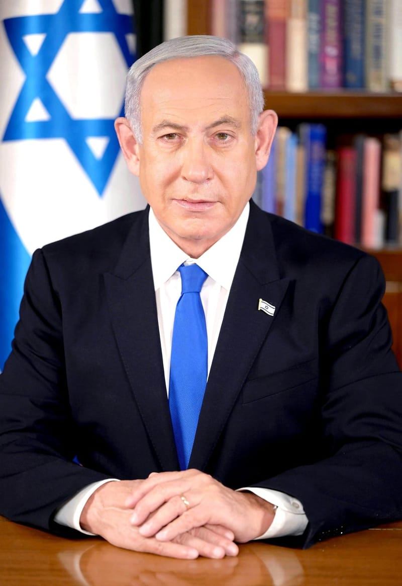 Benjamin Netanyahu, de terno escuro e gravata azul, sentado a uma mesa diante da bandeira de Israel
