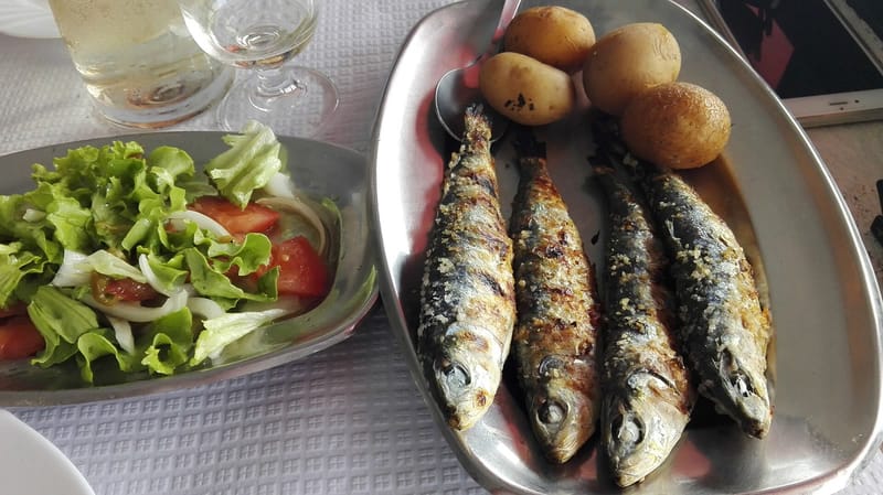 Sardinhas assadas servidas em travessa, ao lado de salada e batatas