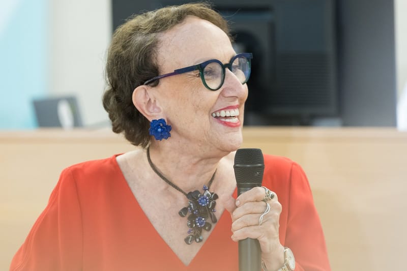 Rebeca Grynspan, de óculos de armação escura e blusa vermelha, sorri ao falar ao microfone