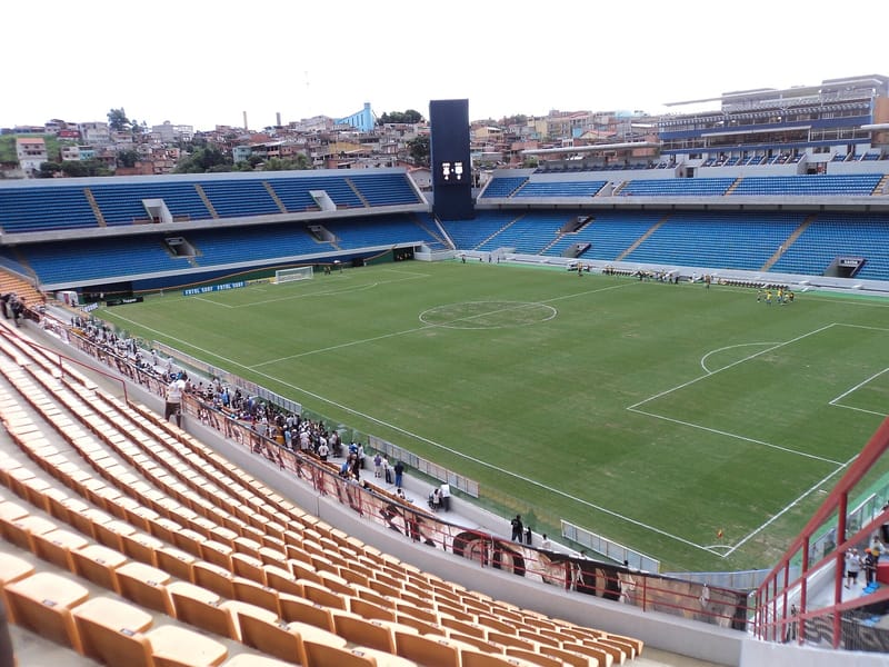 Vista do interior da Arena Barueri, com o gramado, as arquibancadas azuis e o placar ao fundo