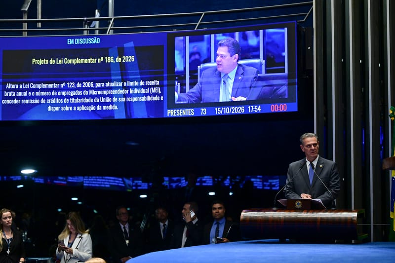 O senador Carlos Fávaro discursa na tribuna do plenário do Senado; no painel acima, o projeto de lei complementar que altera o limite de receita do MEI e concede remissão de dívidas