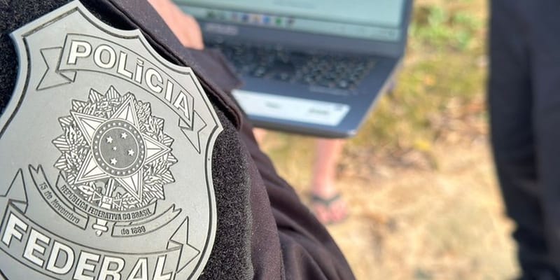 Brasão da Polícia Federal no colete de um agente, com um notebook ao fundo, em imagem de divulgação da corporação
