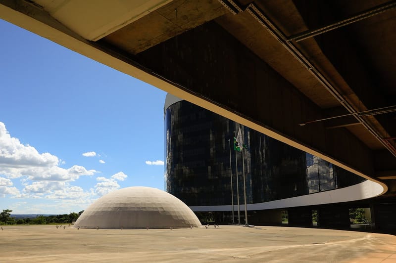 Sede do Tribunal Superior Eleitoral, em Brasília, com prédio de vidro escuro, cúpula de concreto em primeiro plano e céu azul