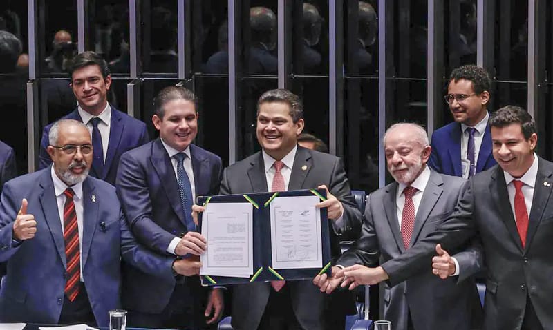 Davi Alcolumbre segura a emenda constitucional assinada, ao lado de Hugo Motta e de Lula, na sessão de promulgação no plenário do Senado