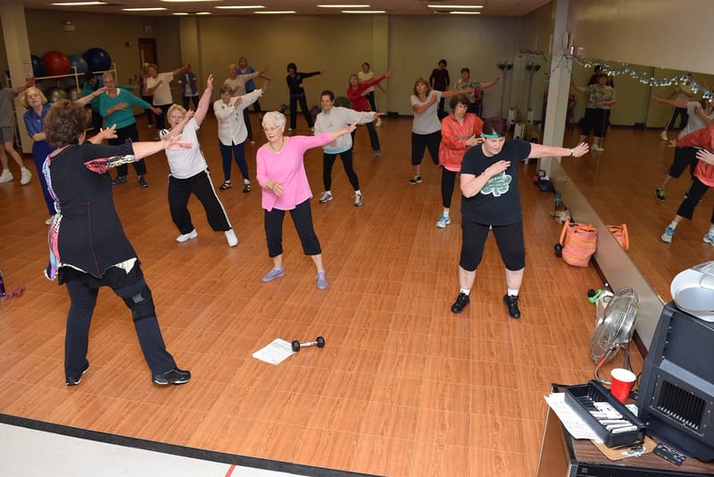 Grupo de idosos faz exercícios de braços em aula de ginástica num centro de convivência