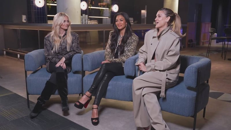 Três integrantes do Pussycat Dolls sentadas lado a lado em sofás azuis durante entrevista, conversando e sorrindo