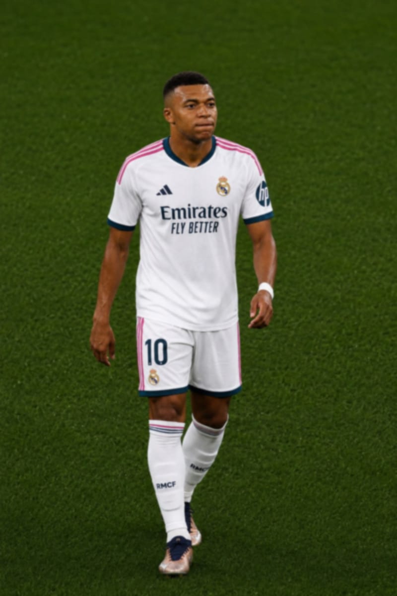 Kylian Mbappé, de uniforme branco do Real Madrid com o número 10 no calção, caminha pelo gramado