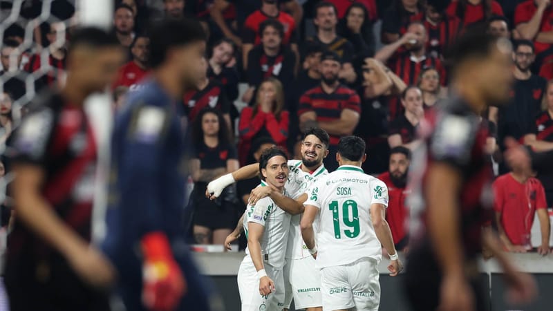 Mauricio, de camisa branca do Palmeiras, sorri abraçado a companheiros depois do gol, com jogadores do Athletico desfocados em primeiro plano e a torcida ao fundo