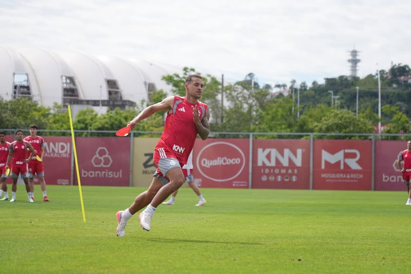 Jogador do Internacional, de uniforme vermelho, corre em treino num gramado, com cones e placas de patrocinadores ao fundo