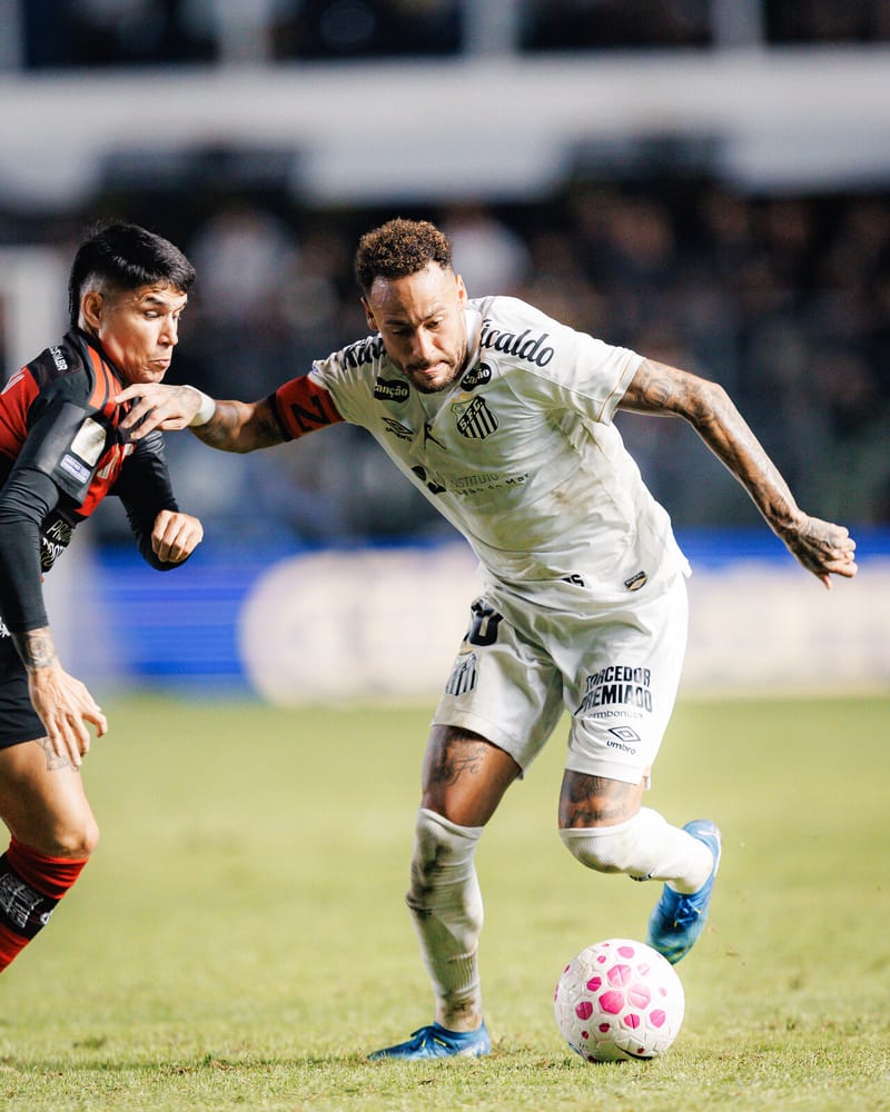 Neymar, de camisa branca do Santos e braçadeira de capitão, conduz a bola e afasta a marcação de um jogador do Flamengo, de rubro-negro, na Vila Belmiro