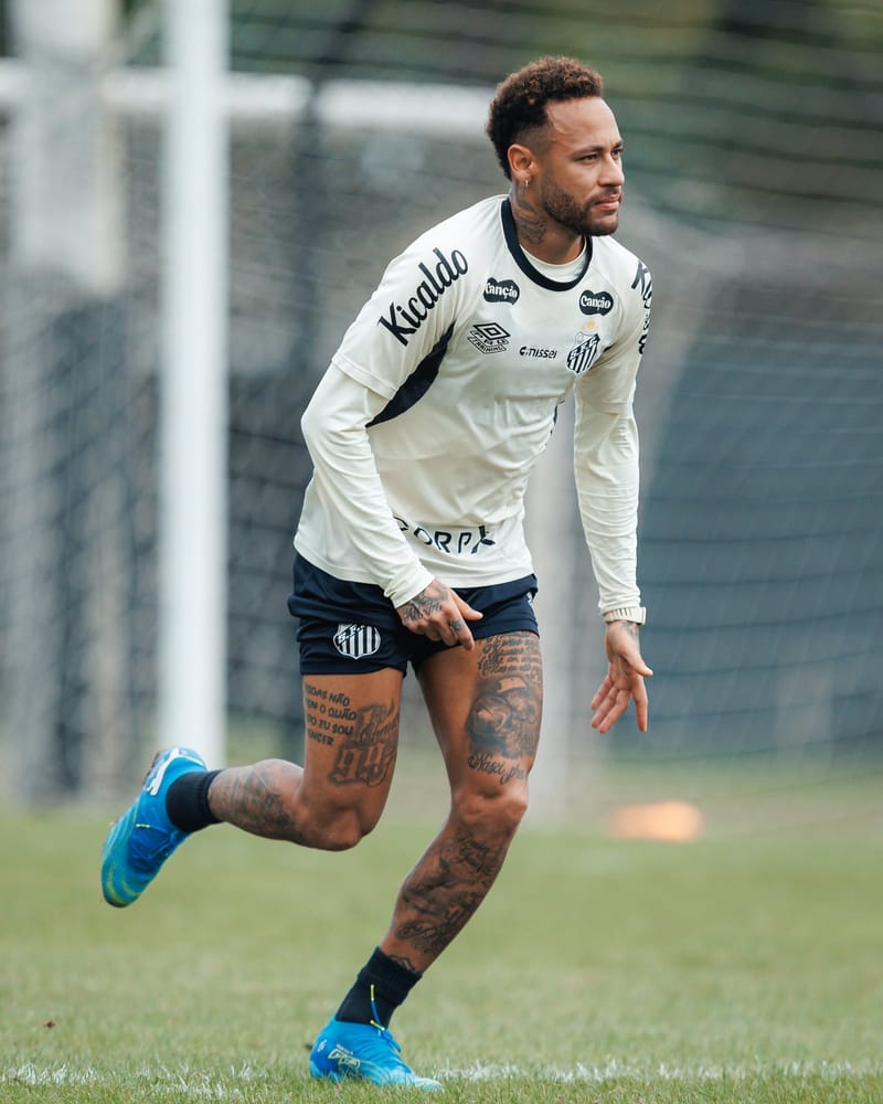Neymar, de camisa branca de treino do Santos e cabelo cacheado, corre em direção à esquerda num gramado, com o gol ao fundo
