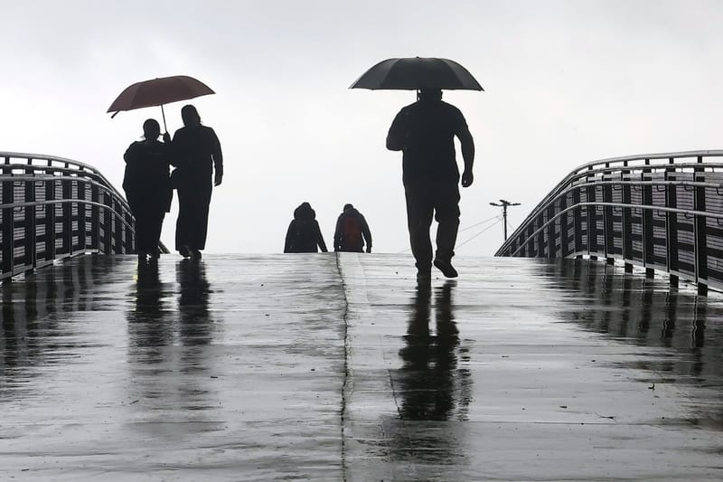 Pedestres com guarda-chuvas atravessam uma passarela molhada sob céu cinzento de chuva em São Paulo