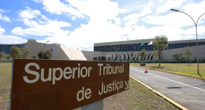Placa do Superior Tribunal de Justiça diante da sede do tribunal, em Brasília, sob céu azul com nuvens