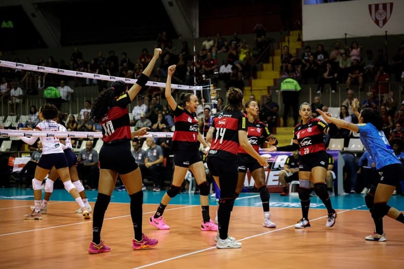 Jogadoras do Flamengo, de uniforme rubro-negro, erguem os braços para comemorar um ponto na quadra