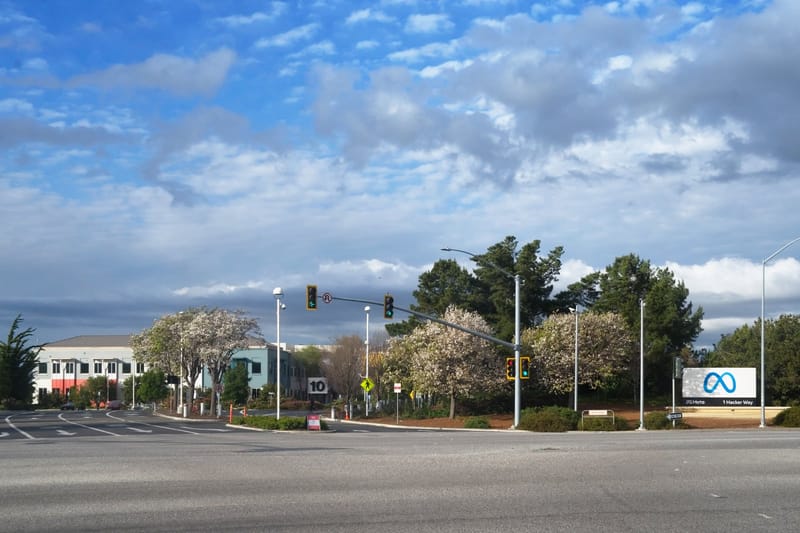 Placa com o logotipo da Meta ao lado de uma rua, com prédios baixos da empresa e árvores floridas ao fundo