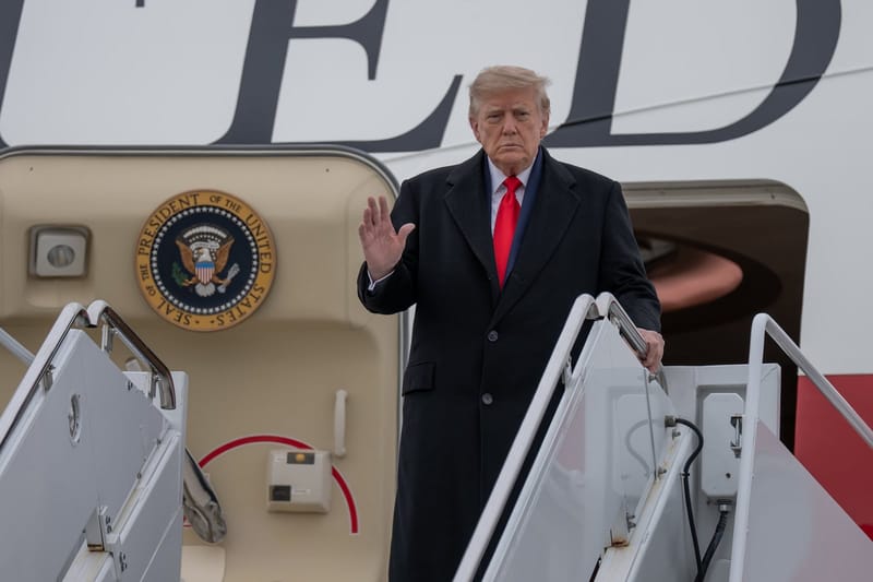 Donald Trump, de sobretudo preto e gravata vermelha, acena no alto da escada do Air Force One, ao lado do selo presidencial