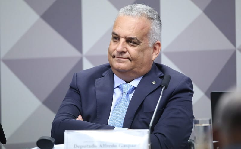 Alfredo Gaspar, de terno azul-marinho e gravata azul-clara, sentado de braços cruzados diante da placa com seu nome em uma comissão do Congresso