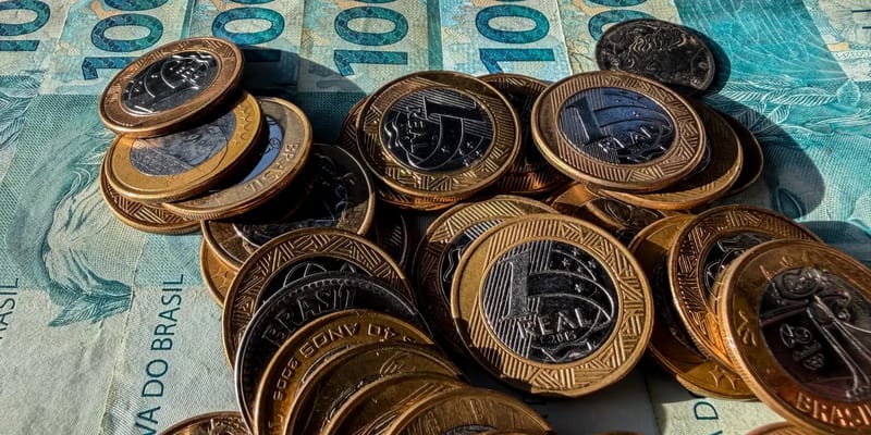 Moedas de um real espalhadas sobre cédulas de cem reais