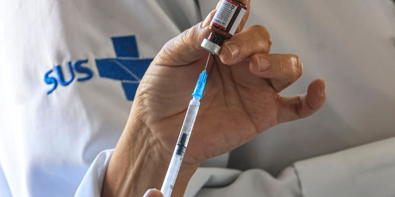 Profissional de saúde com jaleco do SUS prepara seringa com dose de vacina