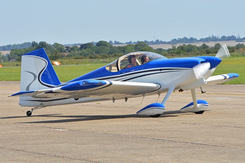 Avião esportivo Van's RV-7 azul e branco taxiando em pista de aeródromo, com dois ocupantes na cabine