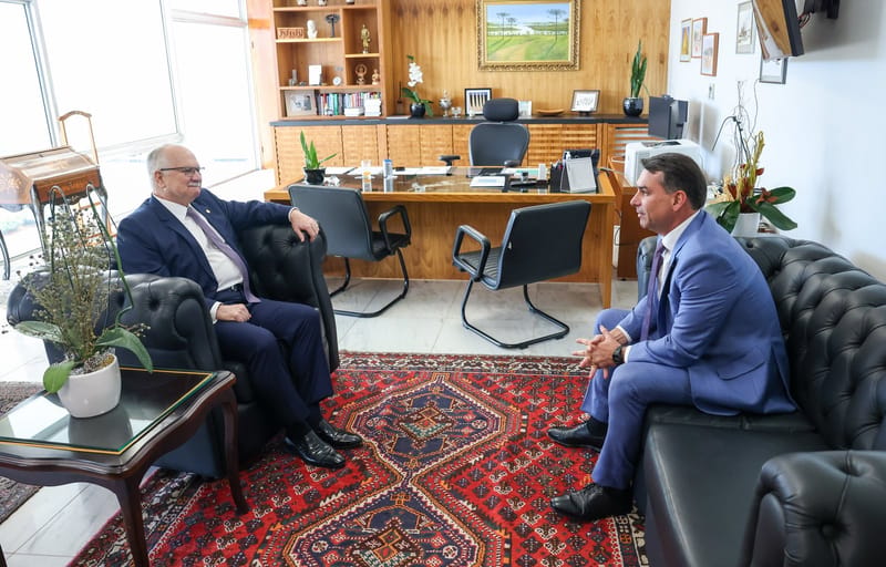 O senador Flávio Bolsonaro, de terno azul, sentado em sofá de couro preto em audiência no STF