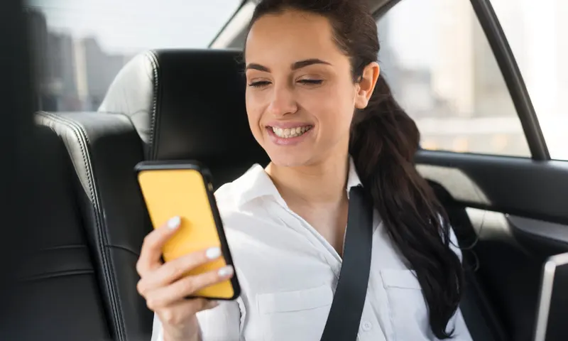 Passageira sorri olhando o aplicativo da 99 no celular, no banco de trás de um carro