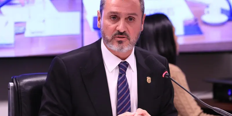 Andrei Rodrigues, de barba grisalha, terno escuro e gravata listrada com distintivo na lapela, fala diante de um microfone