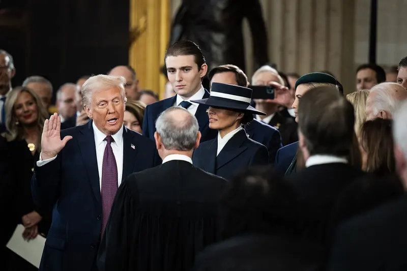 Donald Trump, de terno escuro e com a mão direita erguida, faz o juramento de posse diante de autoridades