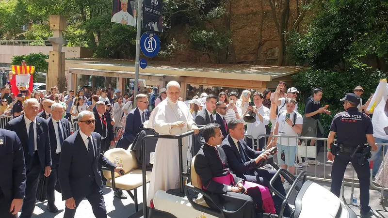 O papa Leão XIV, de branco, acena de um carrinho elétrico cercado por seguranças e fiéis em uma rua da abadia de Montserrat