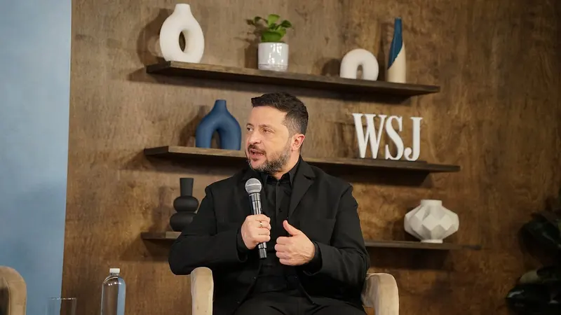 Volodymyr Zelensky, de preto, fala ao microfone e gesticula com a mão direita diante de uma parede de madeira com prateleiras