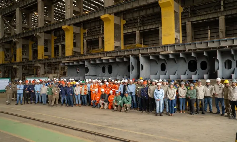 Dezenas de trabalhadores de capacete posam diante de grandes blocos de aço no galpão do Estaleiro Rio Grande, no Rio Grande do Sul