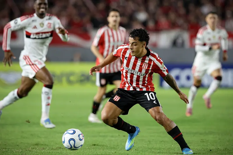 Camisa 10 do Estudiantes, de listras vermelhas e brancas, conduz a bola pressionado por jogadores do Flamengo, de branco, no jogo em La Plata