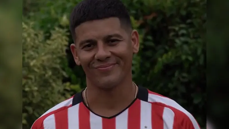 Marcos Rojo sorri vestindo a camisa listrada em vermelho e branco do Estudiantes, com plantas ao fundo