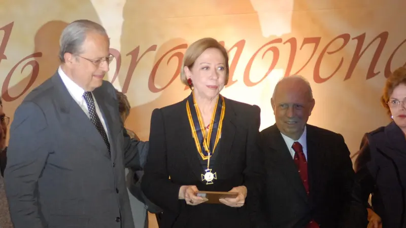 Fernanda Montenegro, de terno preto e medalha no pescoço, segura um estojo durante cerimônia de premiação, ao lado de autoridades