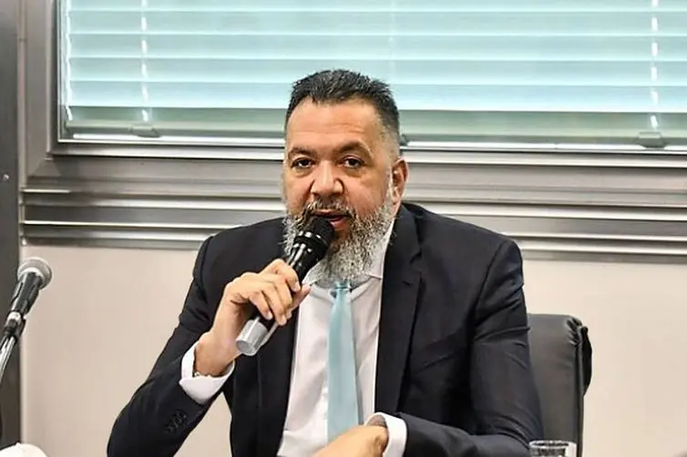 Márcio Canella, de barba grisalha e terno escuro, fala ao microfone sentado a uma mesa