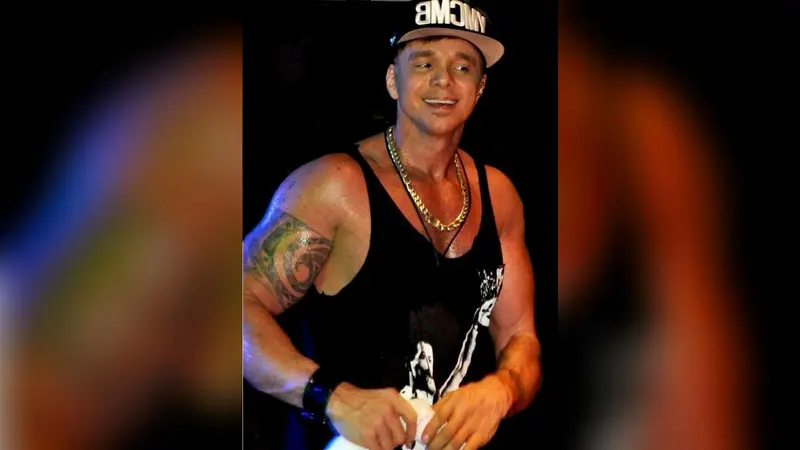 O cantor Netinho sorri no palco, de boné, regata preta e corrente dourada, em show de 2019