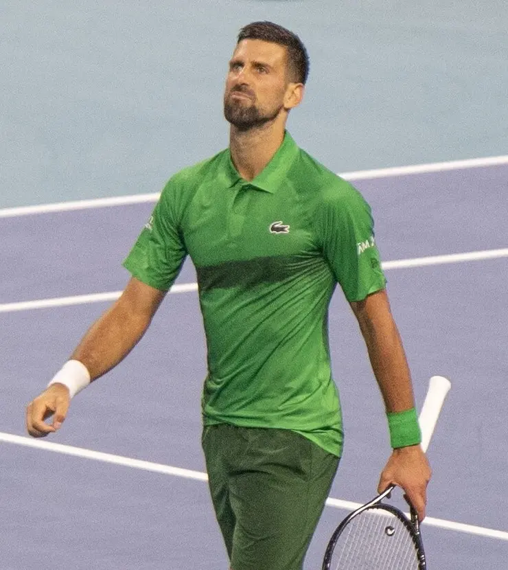 Novak Djokovic, de camisa e bermuda verdes, caminha pela quadra com a raquete na mão no Miami Open de 2025