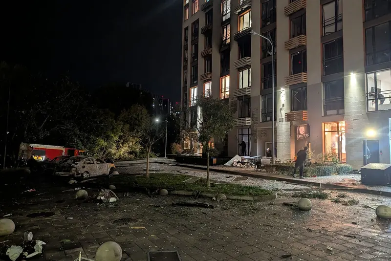 Prédio residencial de Kiev com janelas destruídas, carro queimado e destroços no chão à noite, após ataque de drone