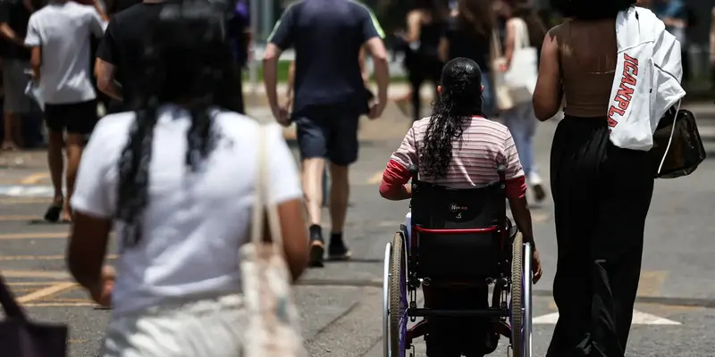 Estudantes caminham de costas em direção ao local de prova do Enem; ao centro, uma jovem em cadeira de rodas