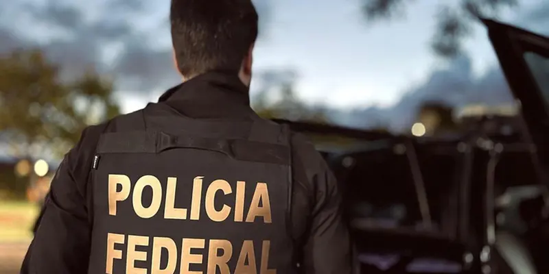 Agente da Polícia Federal, de costas, ao lado de viatura durante operação