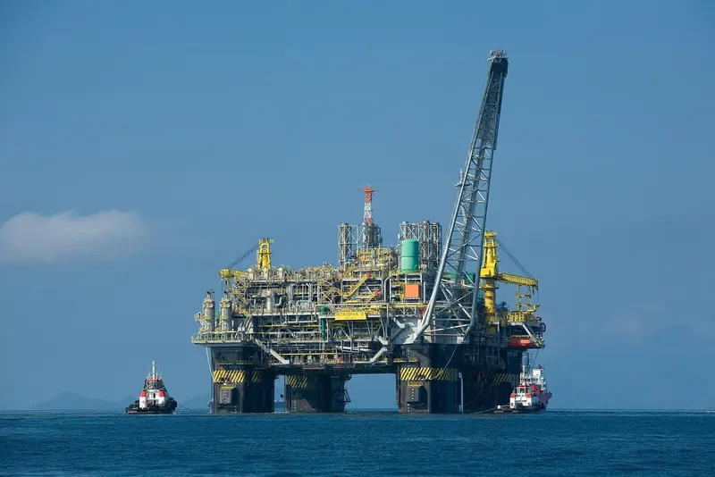 Plataforma de petróleo P-51 da Petrobras no mar, com dois rebocadores ao lado, sob céu azul