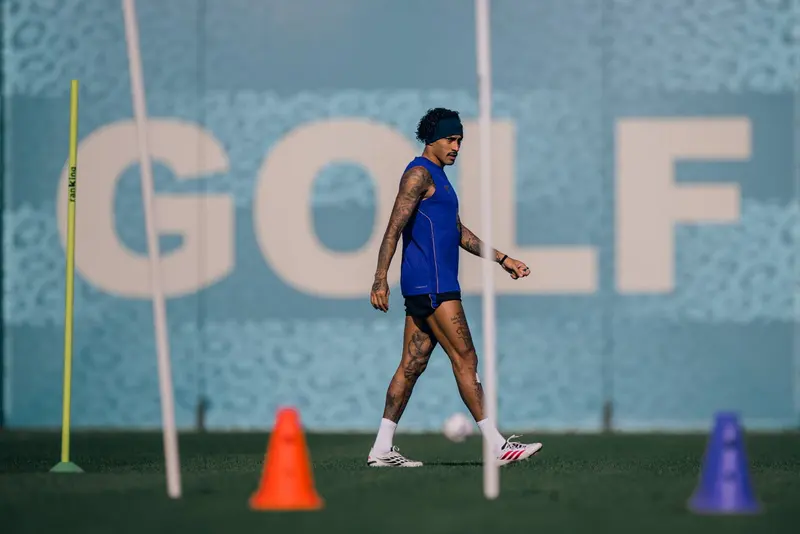 Raphinha, de faixa no cabelo e camiseta azul sem mangas, caminha entre cones no treino do Barcelona