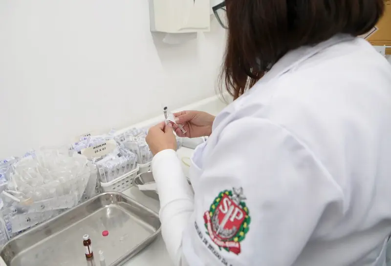 Profissional de saúde de jaleco prepara seringa de vacina em sala de vacinação